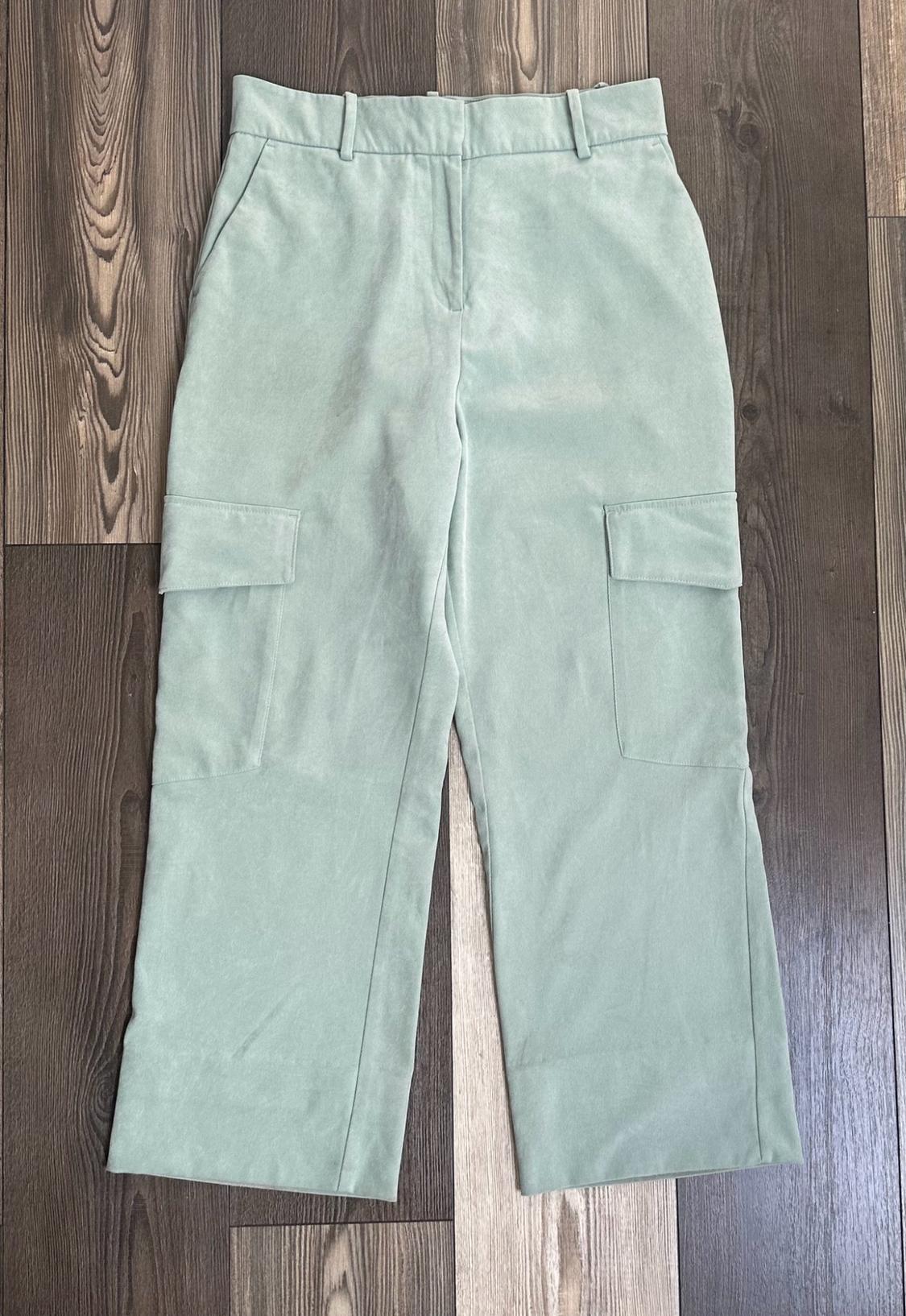 Light green cargo trousers with side pockets, laid out on a wooden floor.