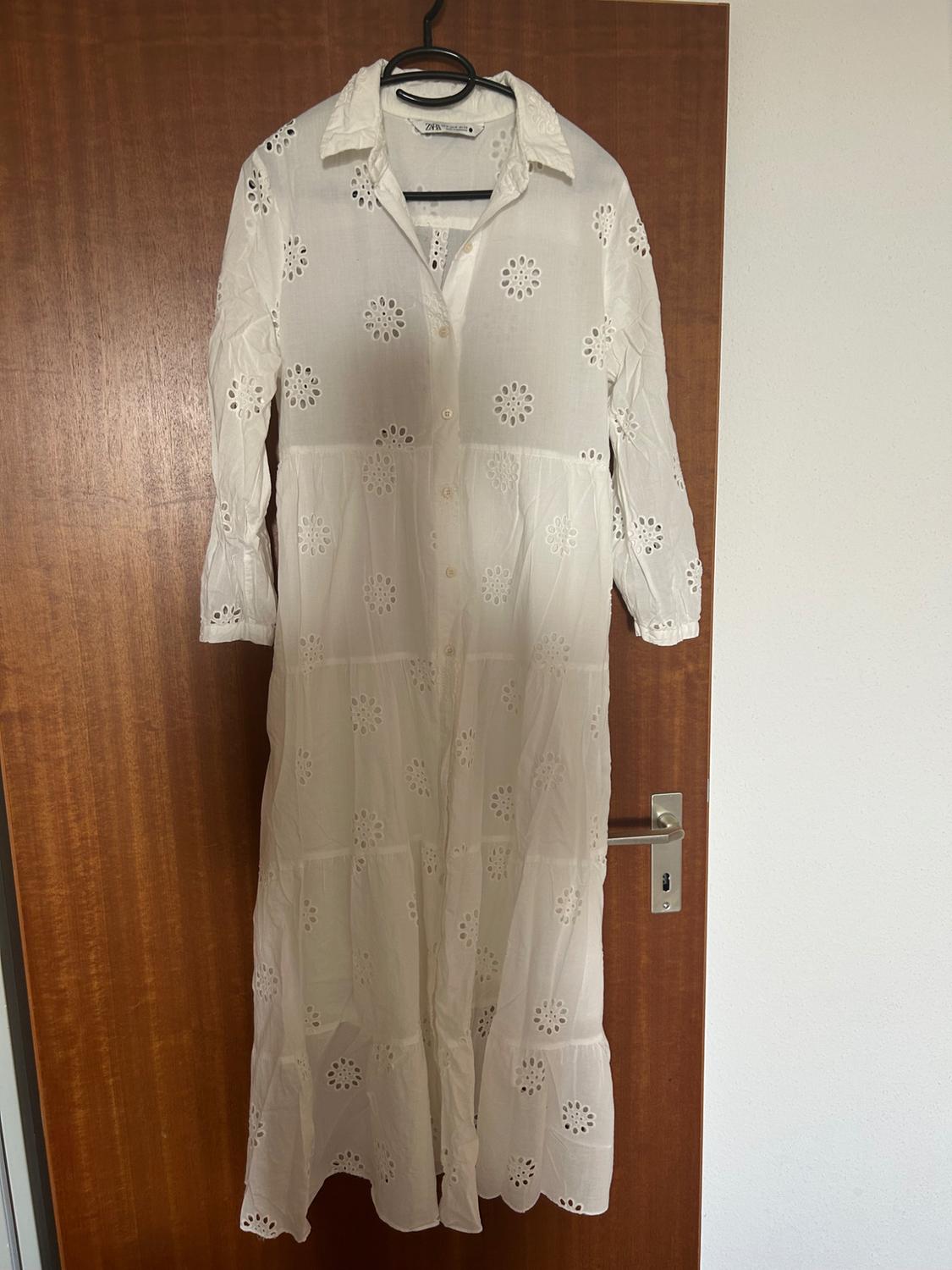Front view of a long white dress with floral embroidery and buttons.