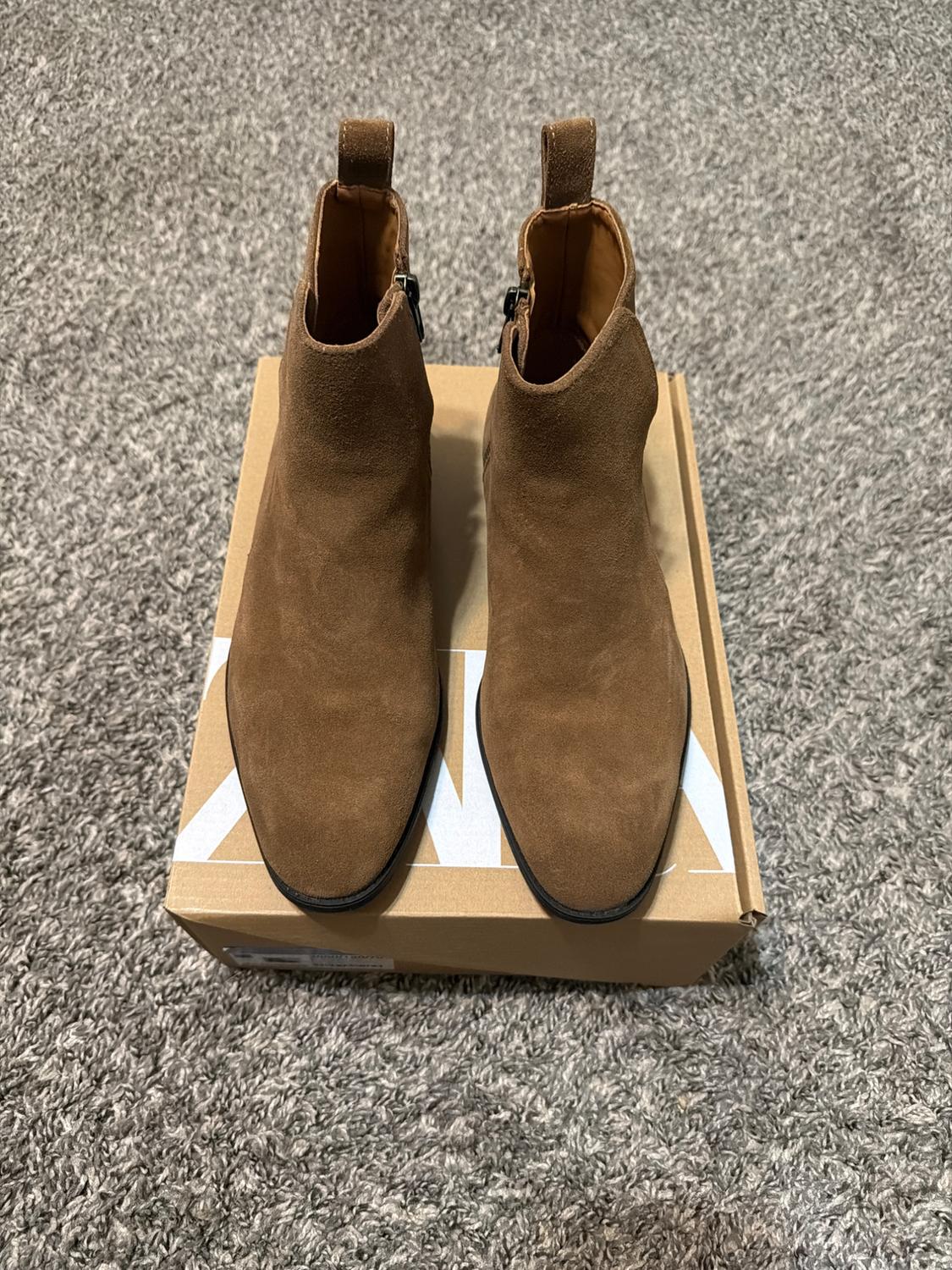Brown suede ankle boots on a cardboard box, placed on a gray rug.