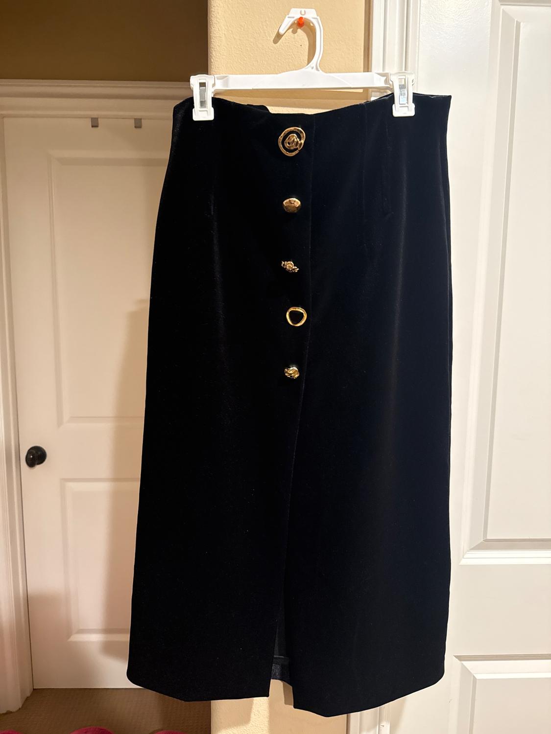 Black velvet skirt hanging on a white hanger, with decorative gold buttons on the front, against a background of white doors.