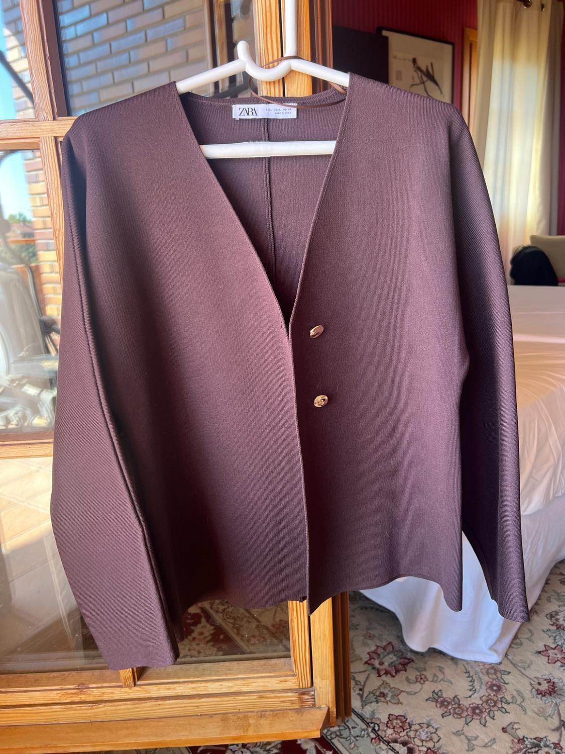 Brown long-sleeved jacket with a V-neck and gold buttons, hanging on a white hanger. Visible text on the label: ZARA.