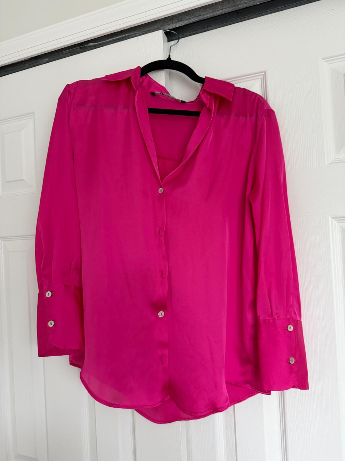 Fuchsia long-sleeved blouse with buttons, hanging on a black hanger on a white door.