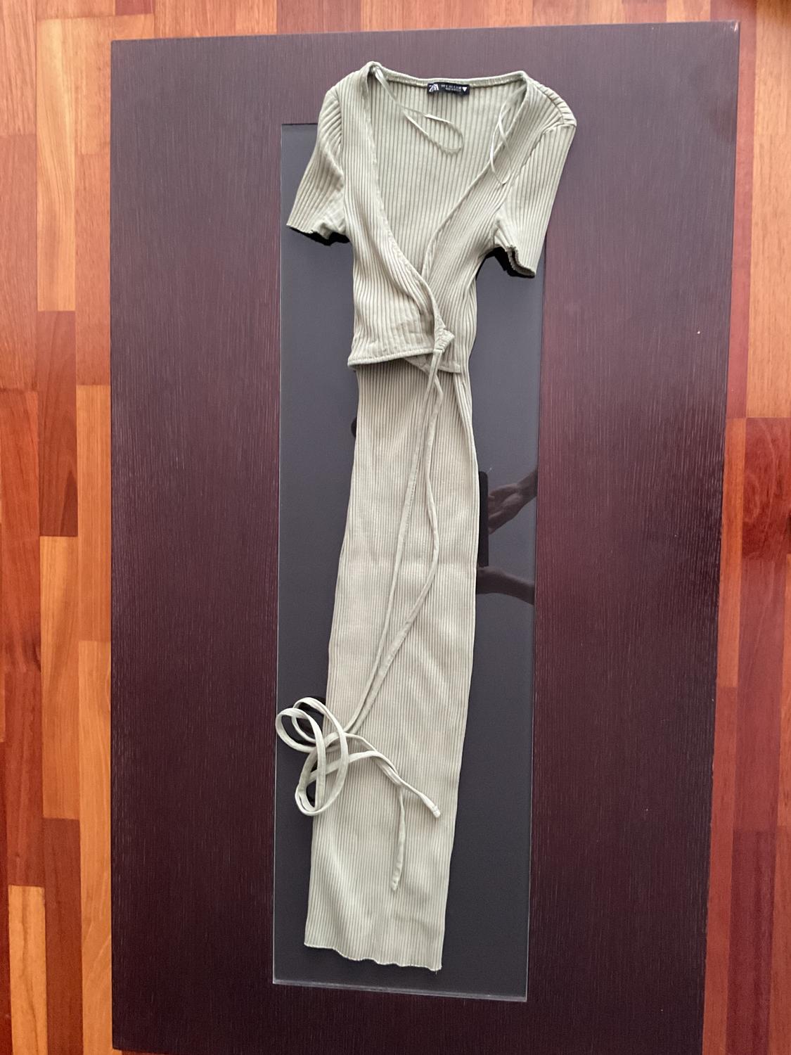 Olive green knitted set with a short-sleeved top and long trousers, on a dark wooden table.