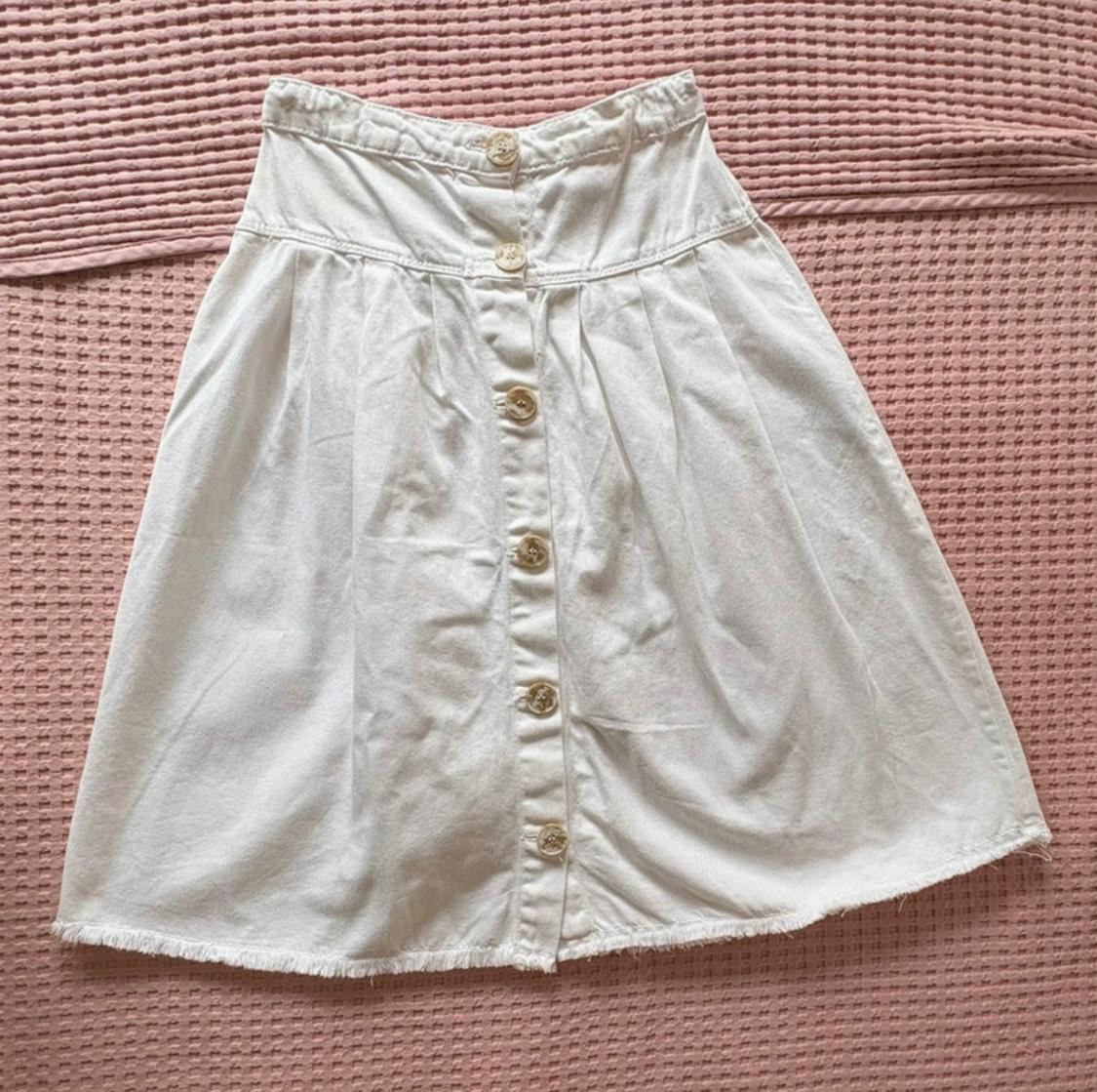 White skirt with front buttons on a textured pink fabric surface.