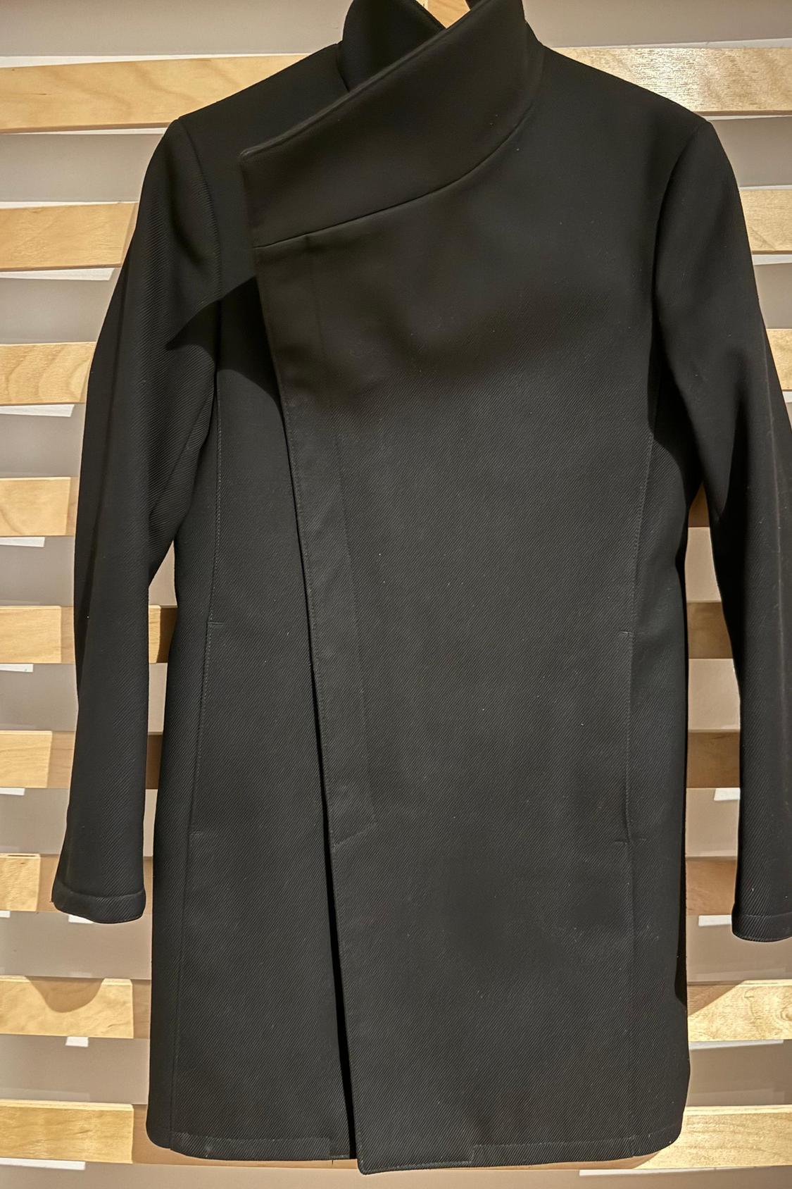 Front view of black coat with asymmetric high collar and wrap-over fastening.