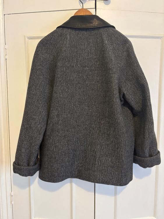 Grey wool coat with a black collar hanging on a wooden hanger in front of a white door.