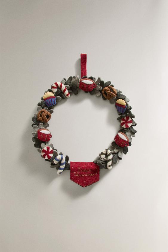 Ukrasni vijenac s ukrasima od slatkiša, šalica i pereca. Tekst "Merry Christmas" na dnu.