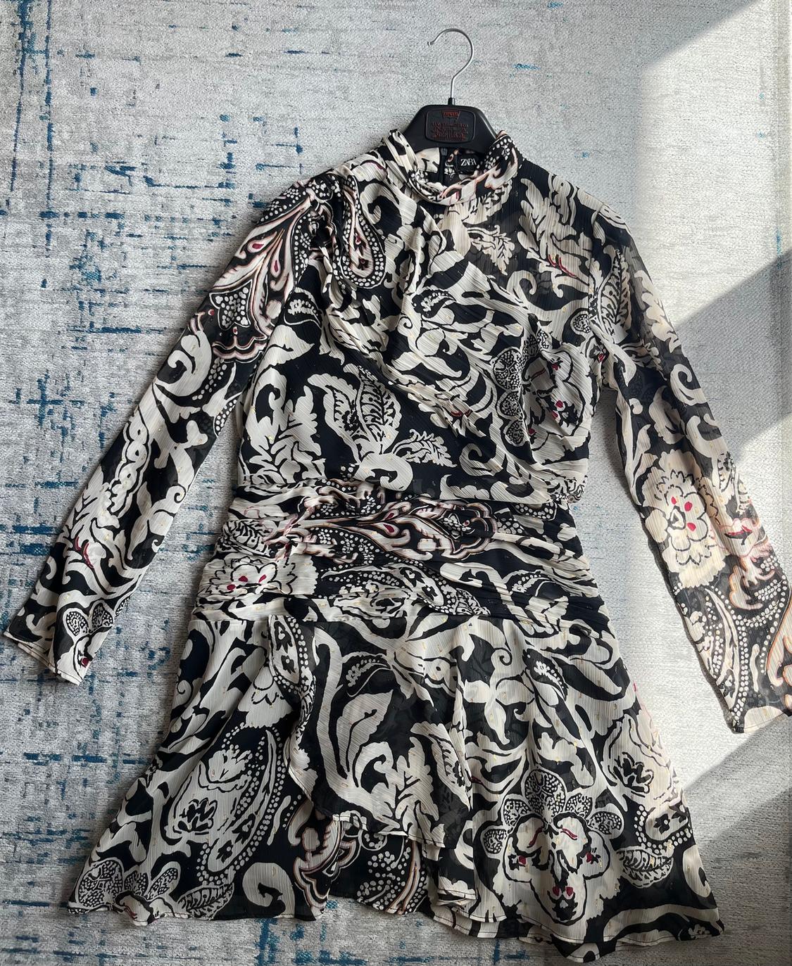 Black and white patterned dress with floral and geometric details, hanging on a hanger over a textured rug.