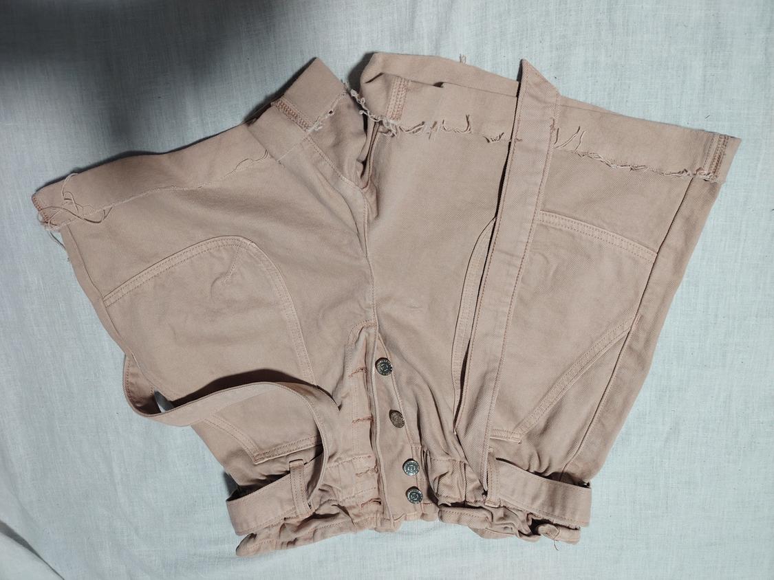 Beige shorts with front buttons and belt, on a white background. Design with frayed edges and large pockets.