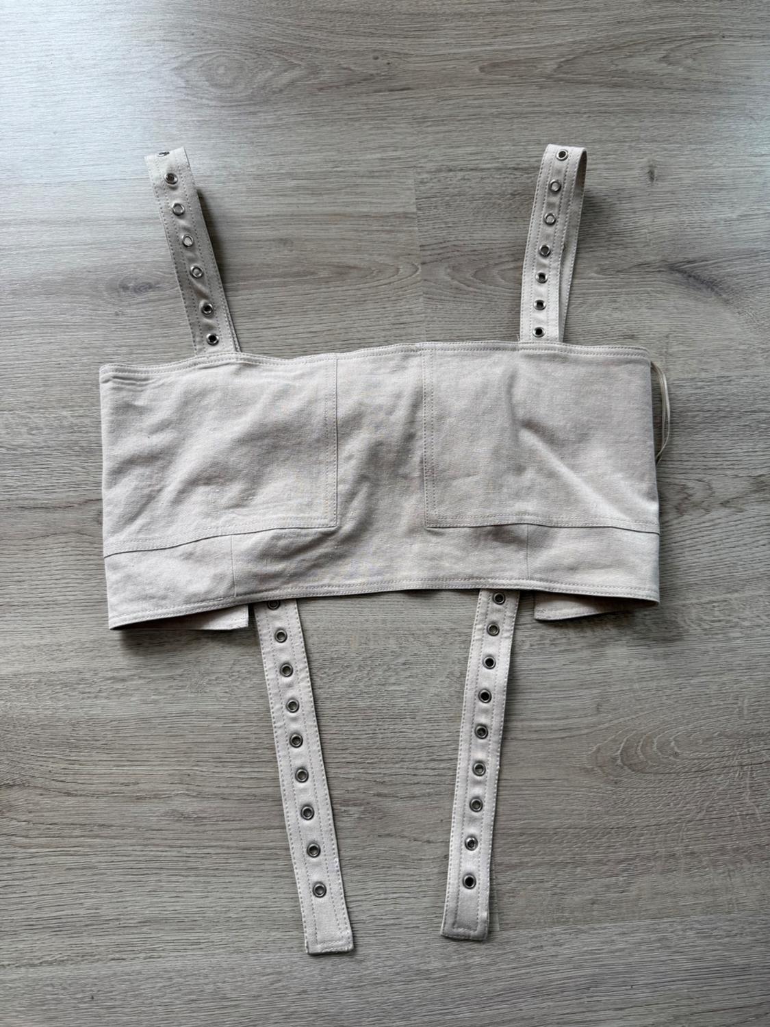 Beige camisole top with adjustable straps and metal eyelets, over a grey wood background.