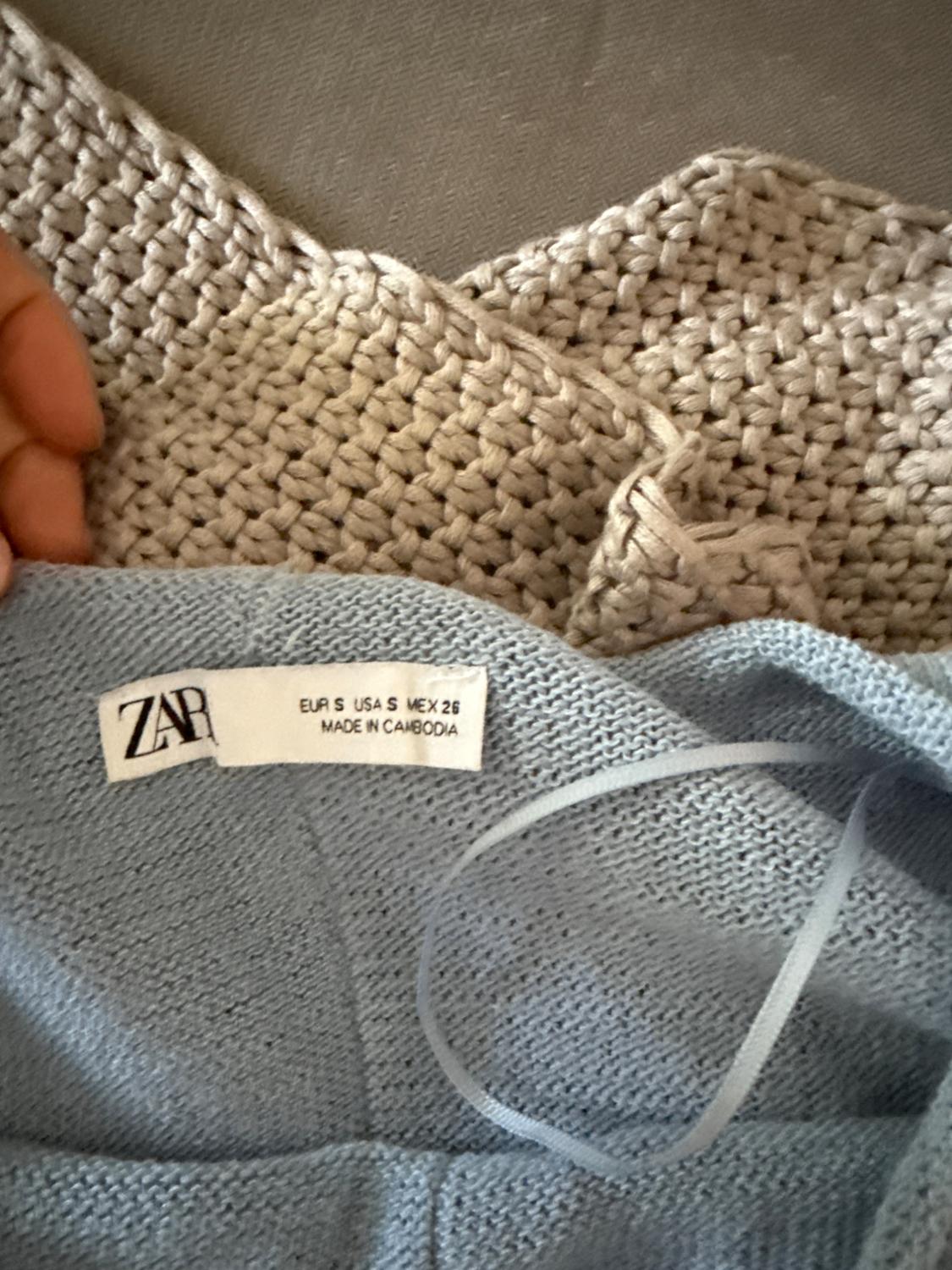 Light blue "ZARA" clothing tag, size EUR S USA S MEX 26, made in Cambodia, on a beige fabric background.