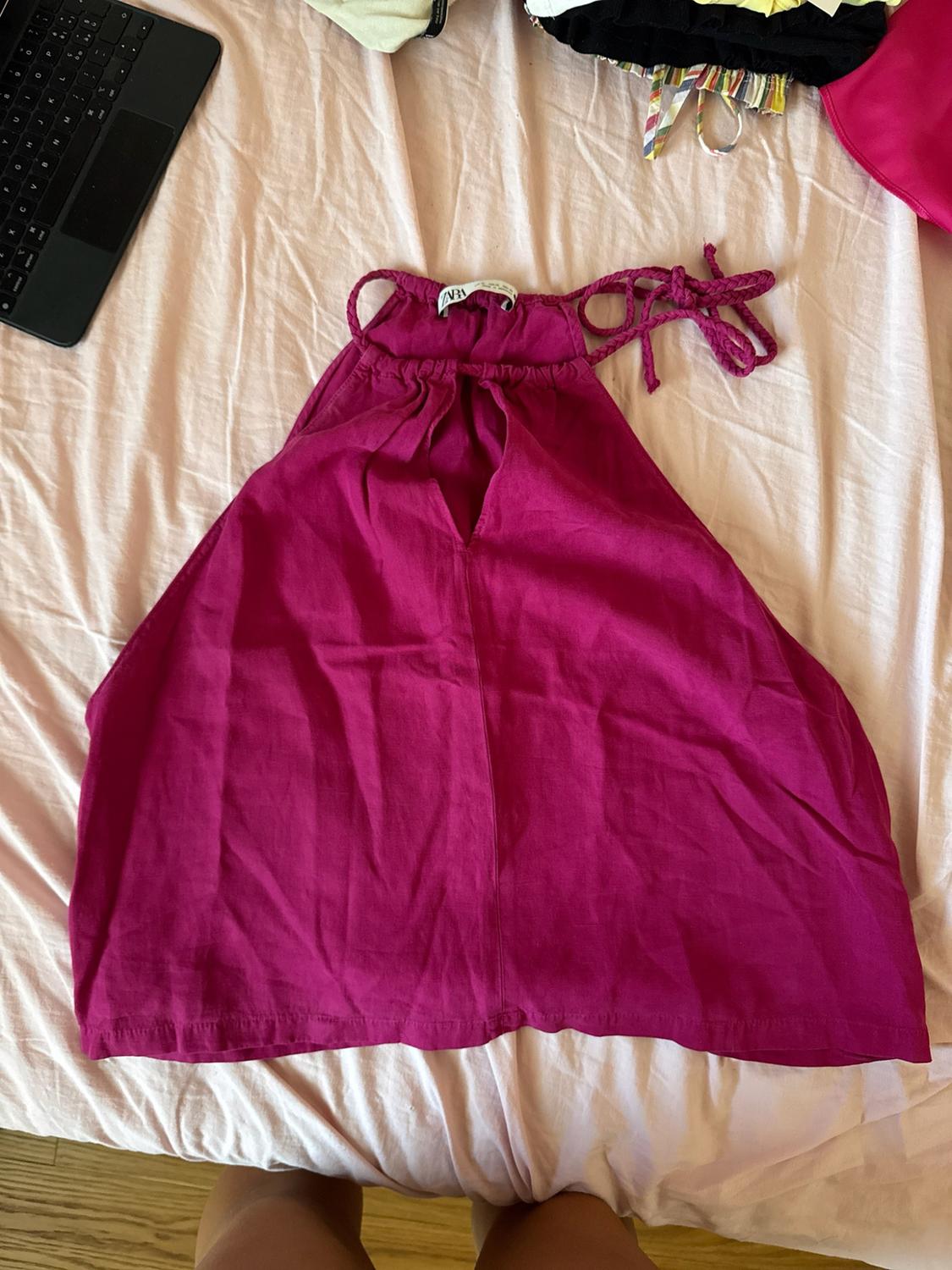 Pink halter-neck top with braided straps on light-coloured sheets. ZARA label. A keyboard and some legs are visible at the edges.