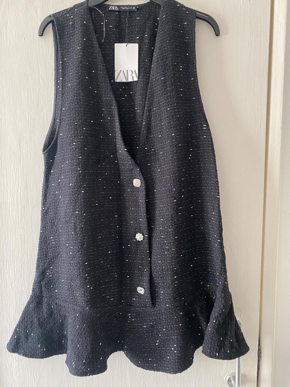 Front view of black waistcoat with decorative buttons and frill detail on the hem.