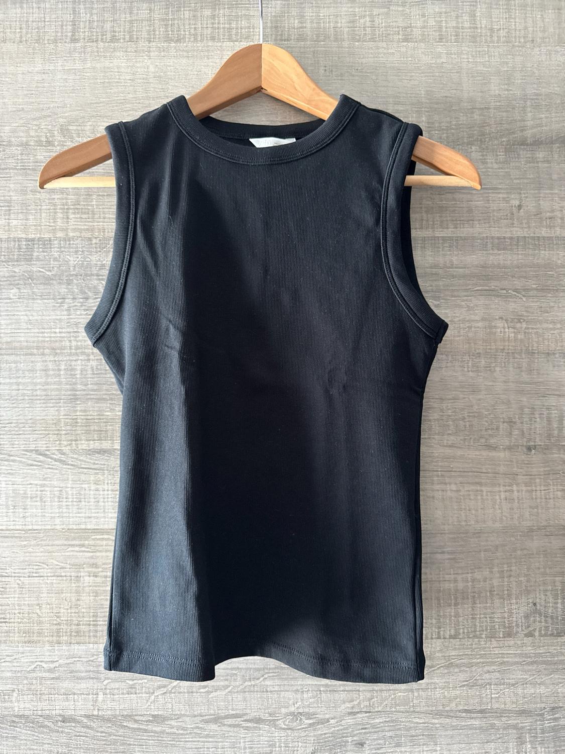 Black ribbed vest top hanging on a wooden hanger against a light wood background. Casual and relaxed style.