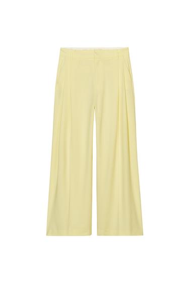 Front view of yellow pleated pants with side pockets.