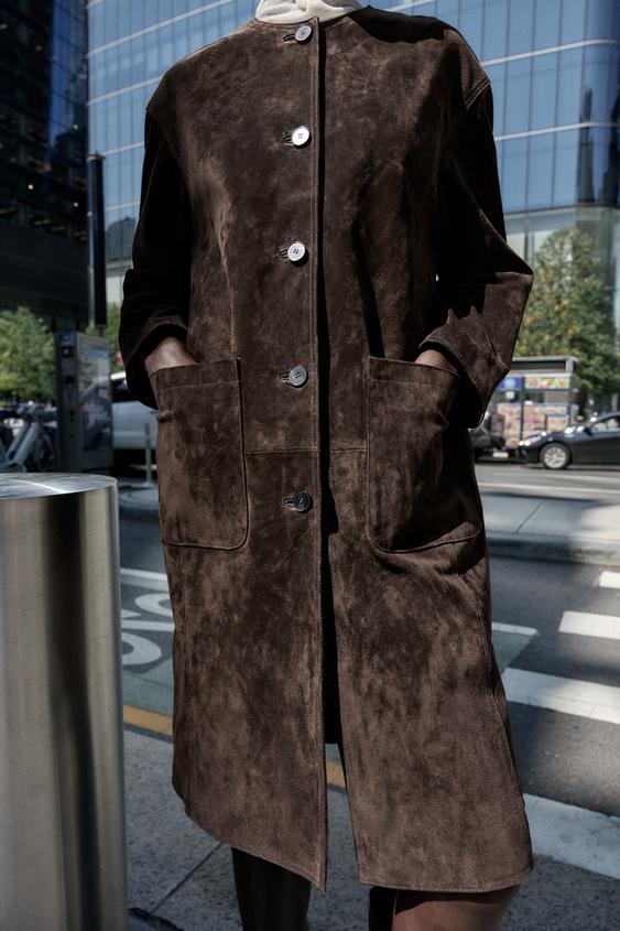 Hladký hnědý kabát střední délky s kulatým výstřihem, dlouhými rukávy, předními nakládanými kapsami a předním zapínáním na knoflíky.