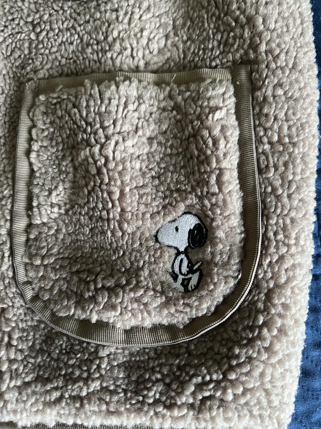 Beige furry fabric pocket with a black and white cartoon character embroidered on a blue background.