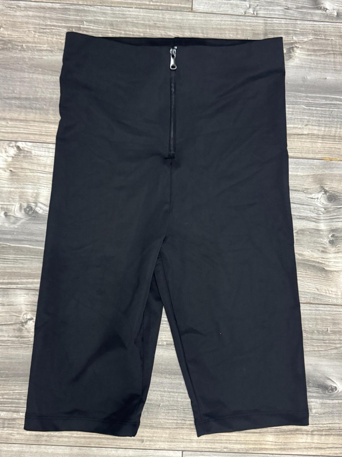 Fitted black high-waisted shorts with a front zip, against a wooden background.