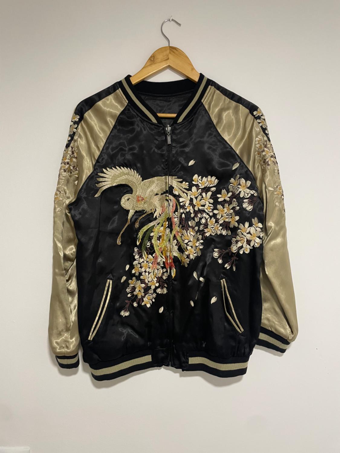 Front view of a black jacket with bird and flower embroidery, gold sleeves and side pockets.