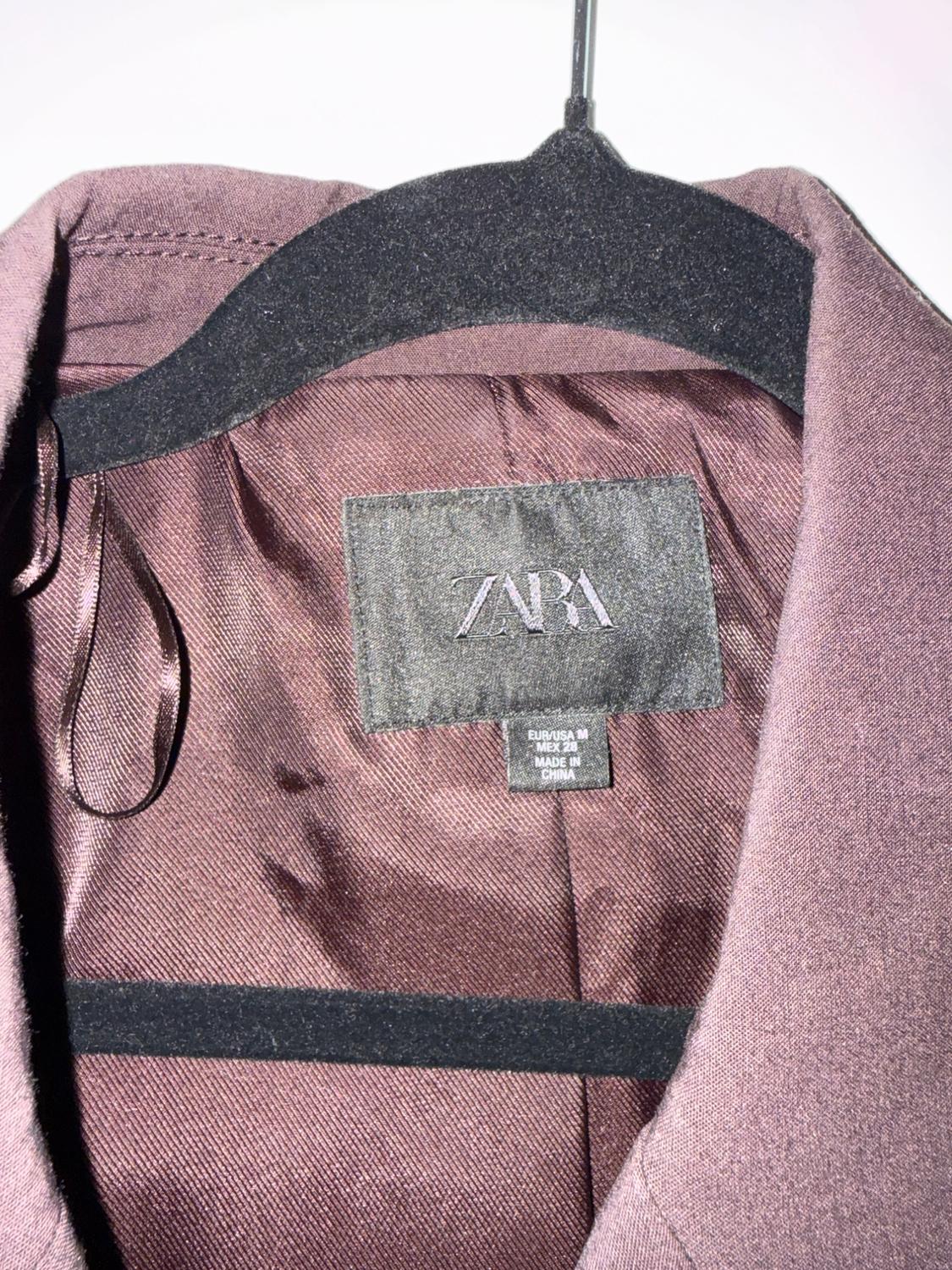 Detail of the lining of a purple jacket on a black hanger. Label with text: ZARA EUR/USA M MEX 28 MADE IN CHINA.