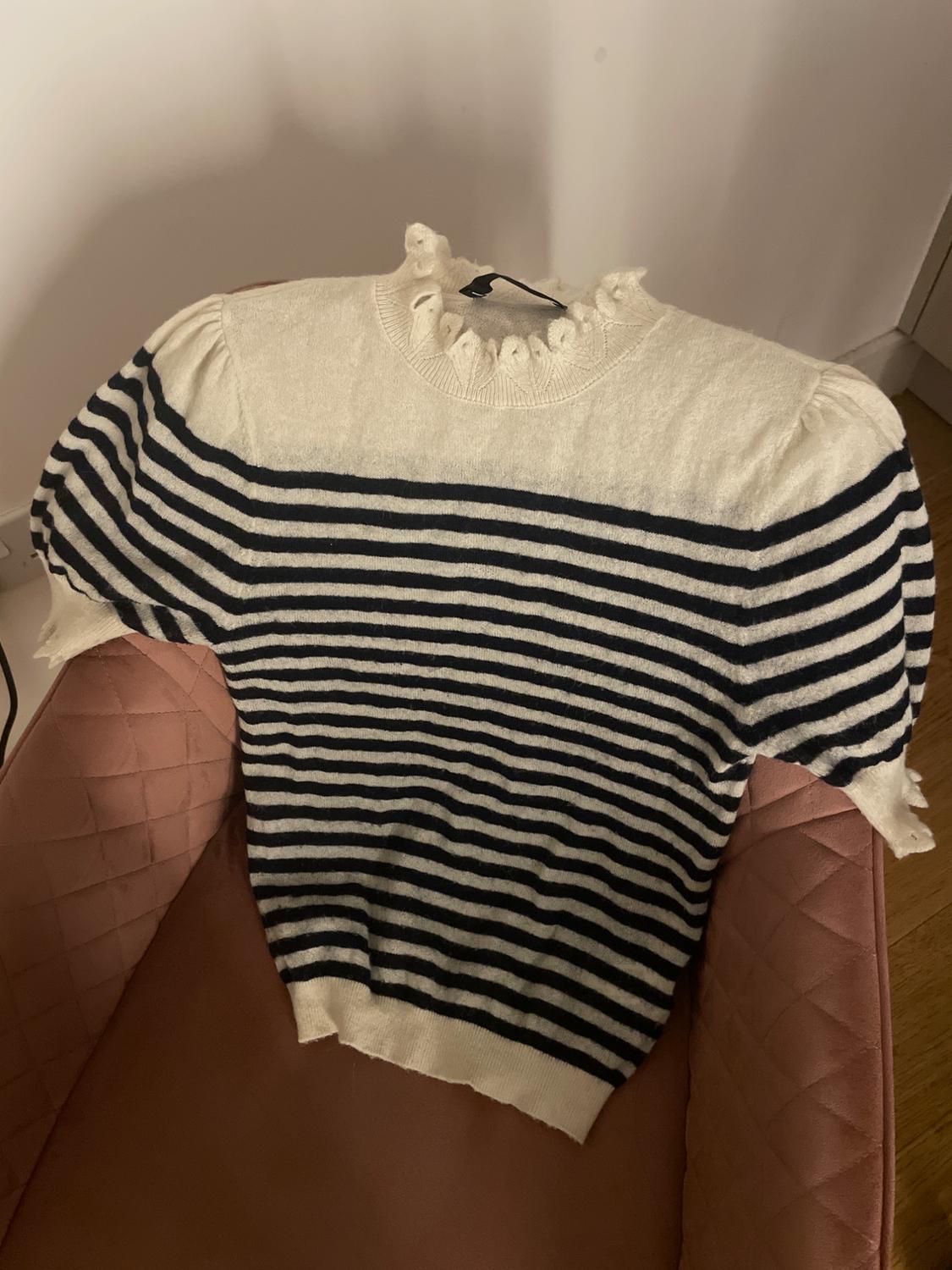 Black and white striped jumper with a ruched neck, placed on a pink upholstered chair in an indoor setting.