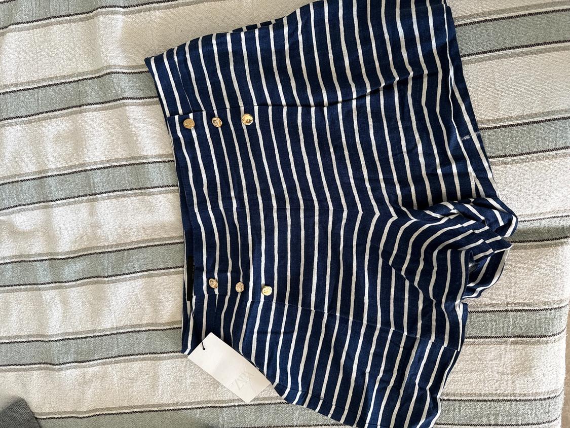 Blue and white striped shorts with gold buttons on a grey and white striped fabric. Visible label.
