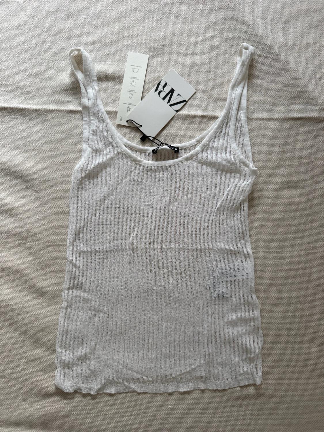 White semi-sheer ribbed vest top over a light fabric background. Label with the text Zara.