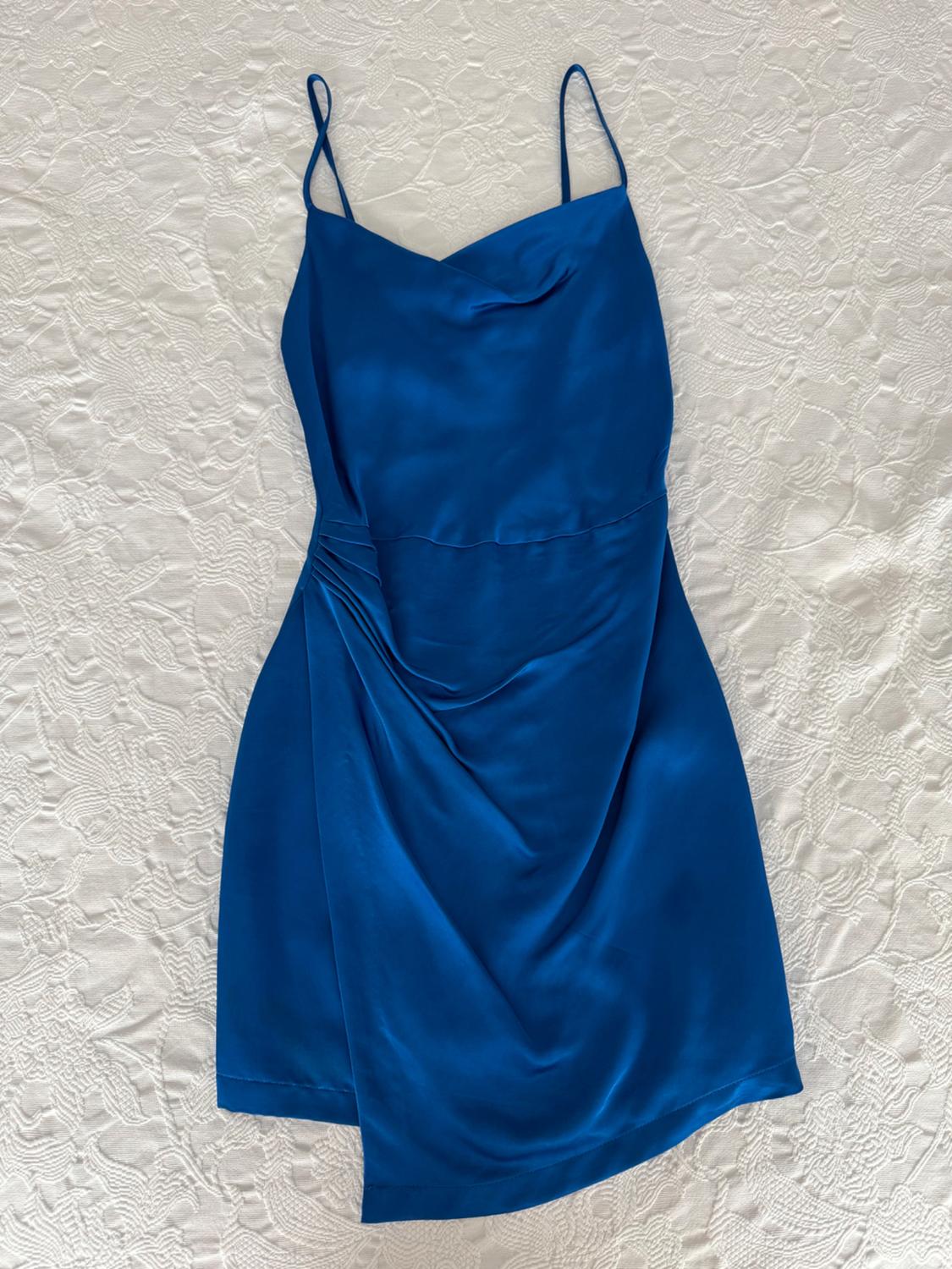 Short blue satin dress with spaghetti straps, a draped neckline, and side ruching, over a white lace background.
