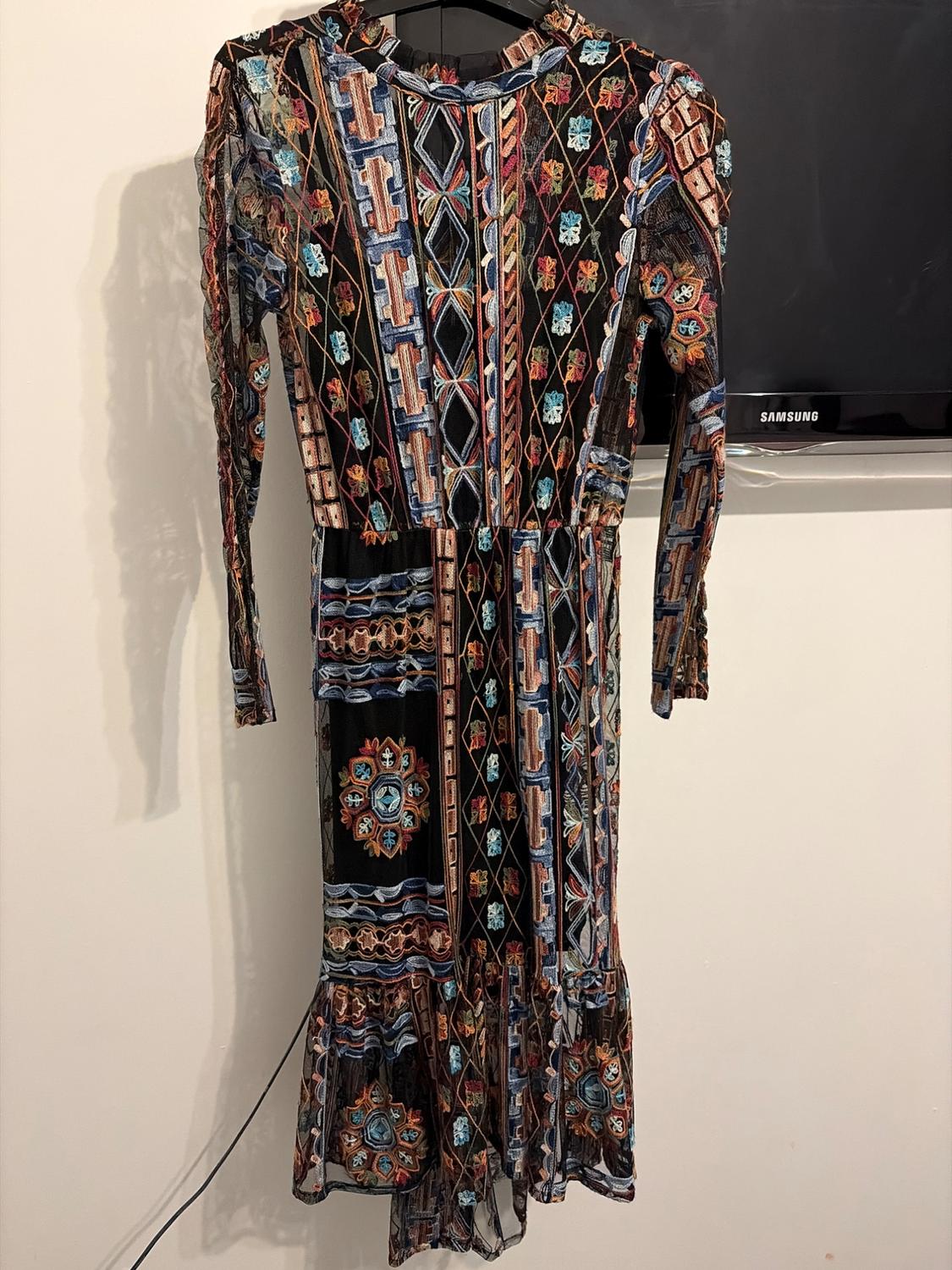 Long-sleeved dress with geometric and floral print in blue, red, and black tones, hanging on a hanger against a white background.