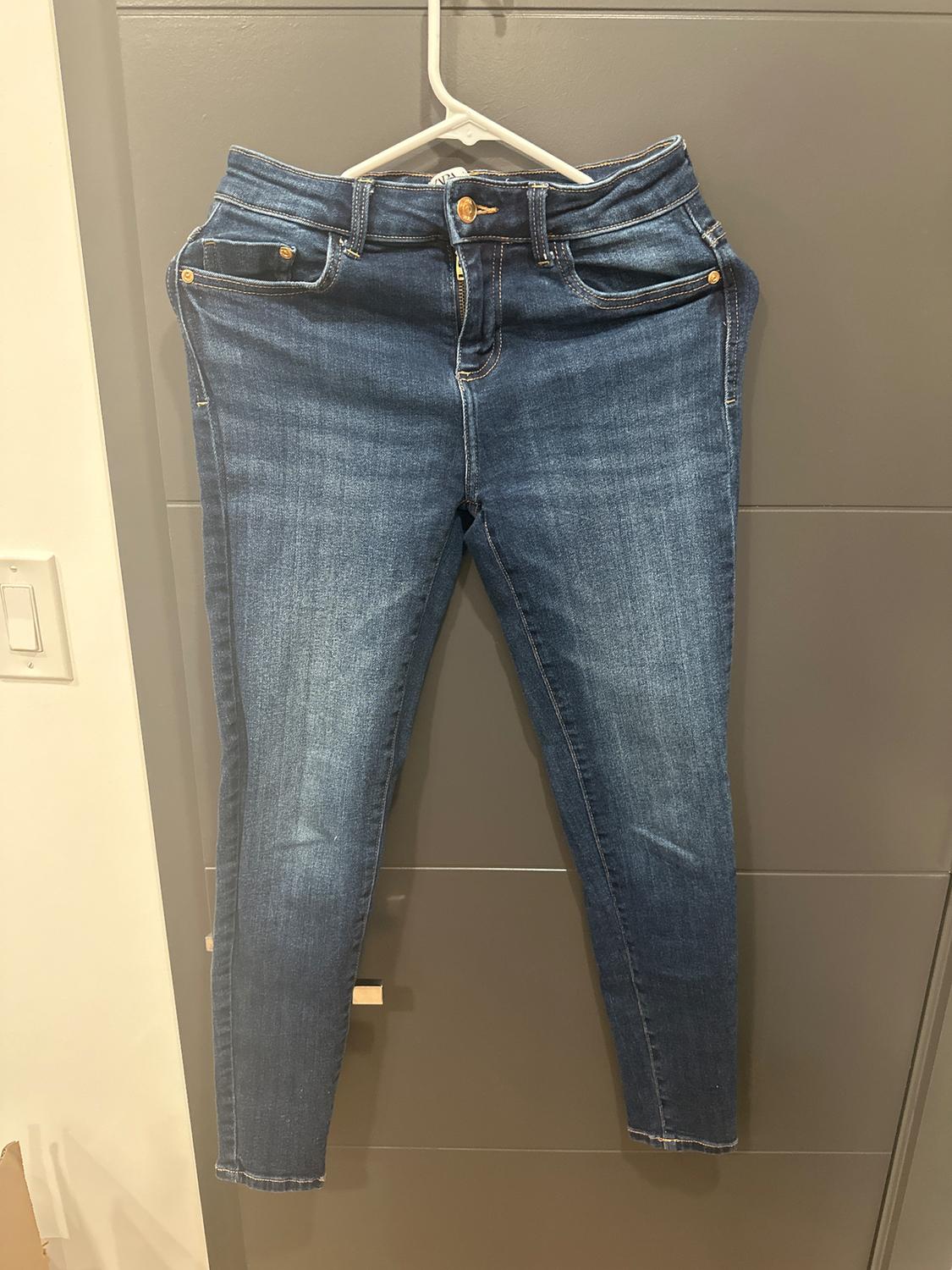 Dark blue jeans hanging on a white hanger over a gray door. Classic design with pockets and a gold button closure.
