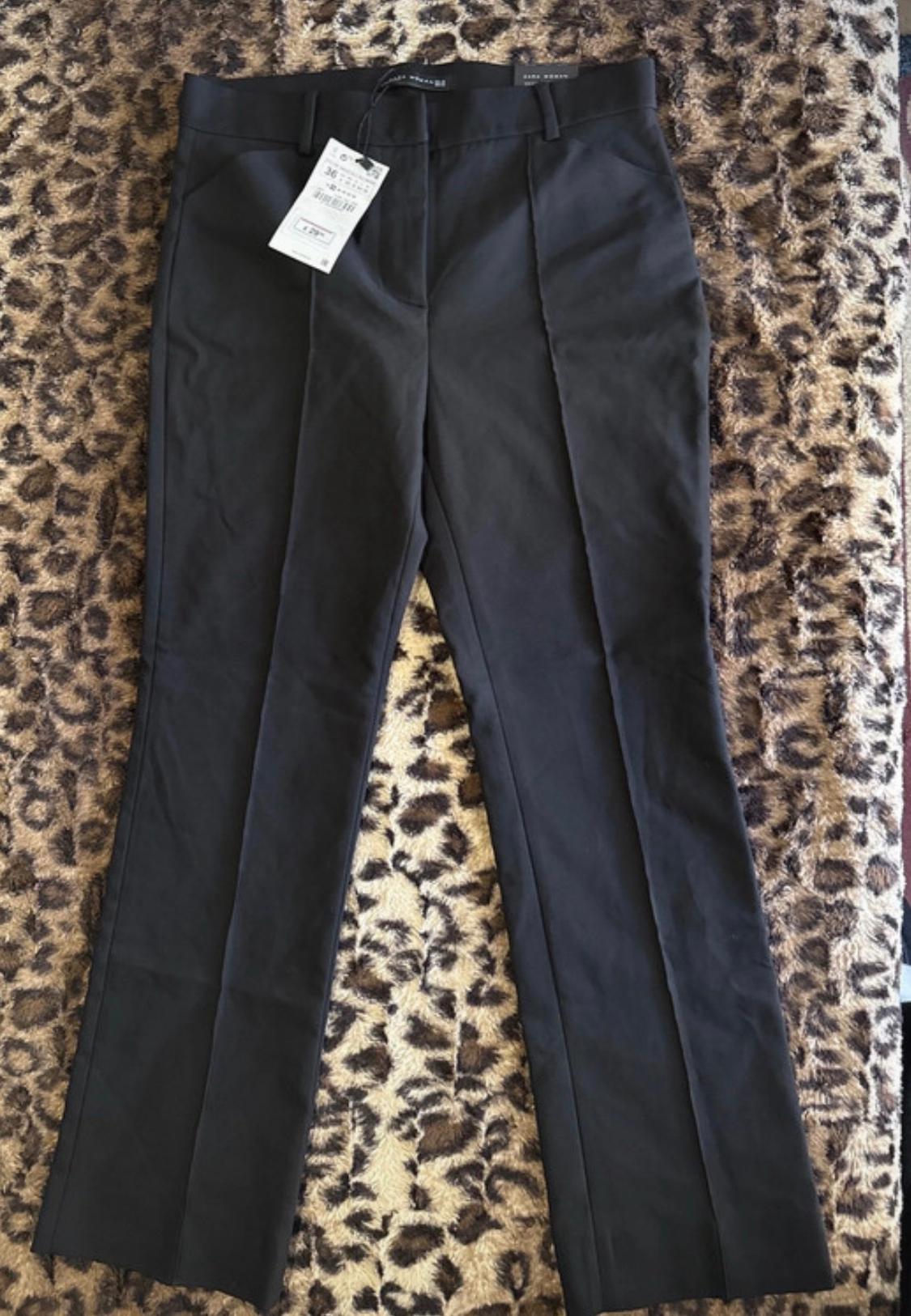 Μαύρο παντελόνι με μπροστινή ρίγα και ετικέτες, απλωμένο πάνω σε φόντο με λεοπάρ μοτίβο.