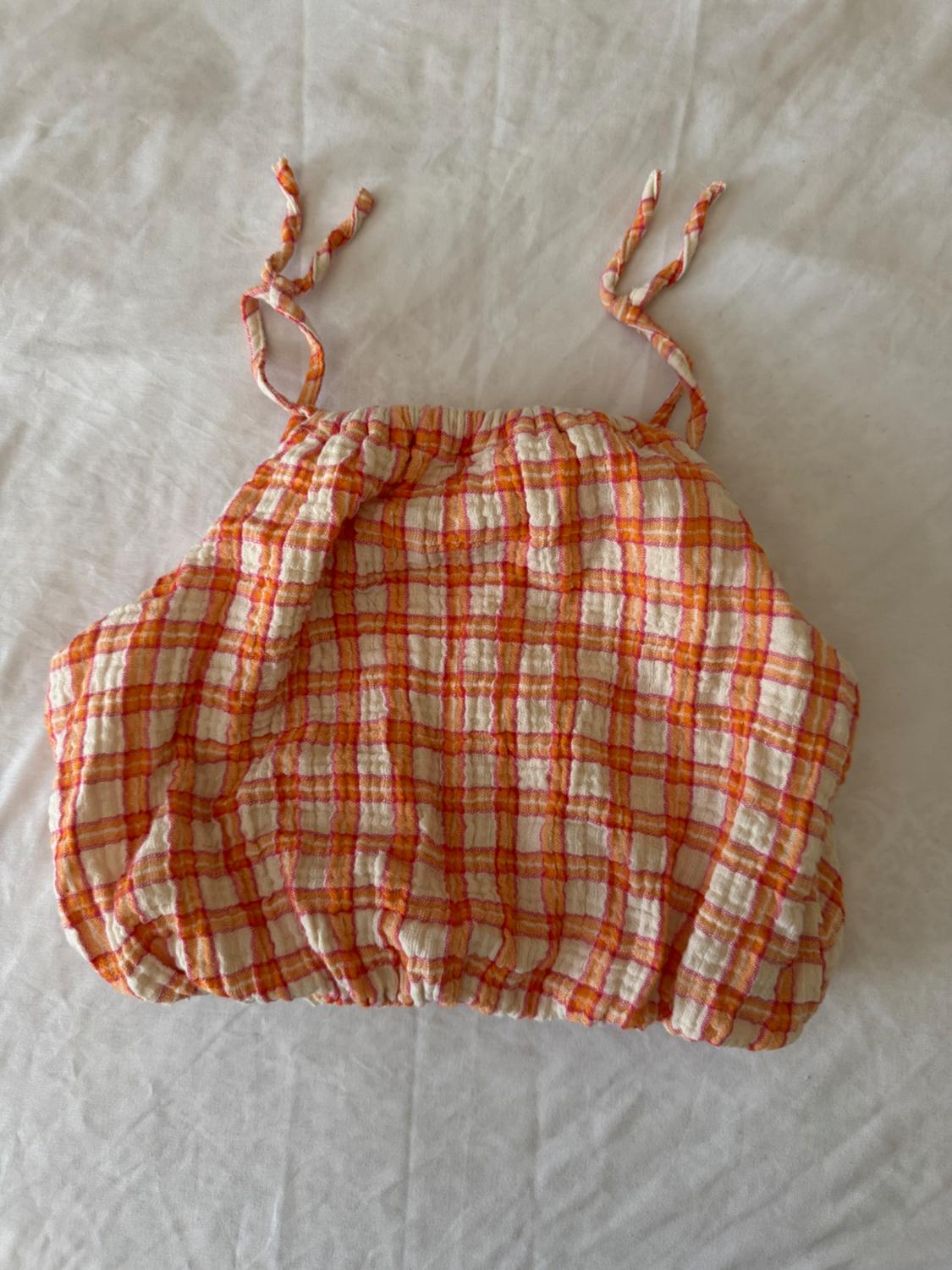 Close-up of an orange camisole top with a checkered design. Elastic at neckline and hem.