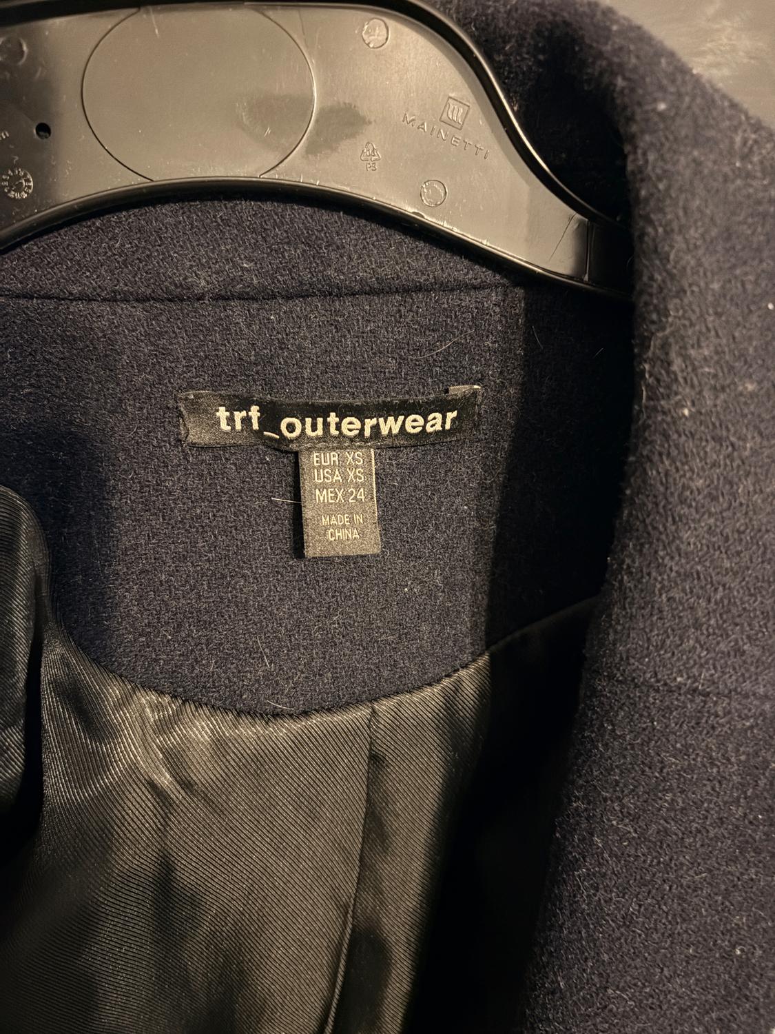 Black "trf_outerwear" coat label on black hanger. Sizes: EUR XS, USA XS, MEX 24. Made in China. Visible black inner fabric.