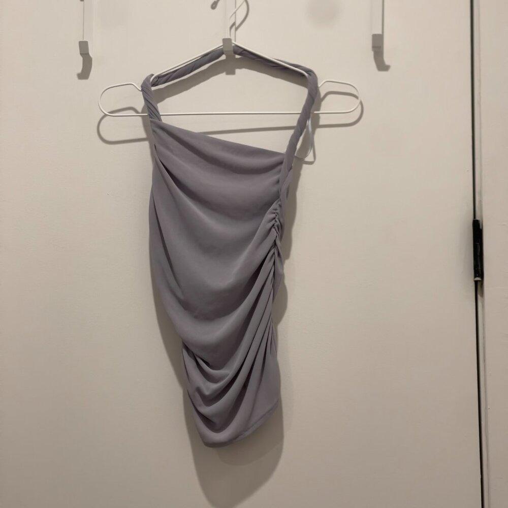 Top in gray tank-style with a draped, ruched side design, hanging on a white hanger over a white door.