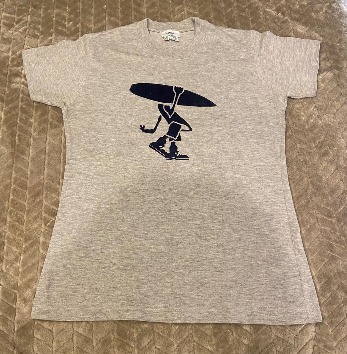 Front view of a grey t-shirt with a print of a figure carrying a surfboard.