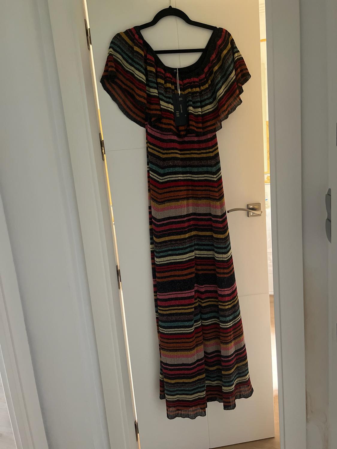Multicoloured striped maxi dress with a frilled neckline, hanging from a hanger on a white door in a relaxed setting.