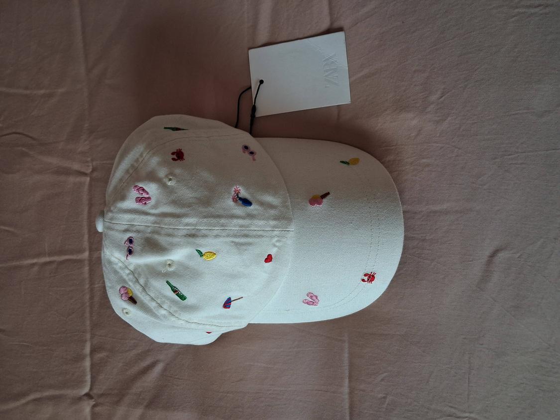 White cap with small colourful embroidery on crinkled light pink fabric. Label with the text ZARA.