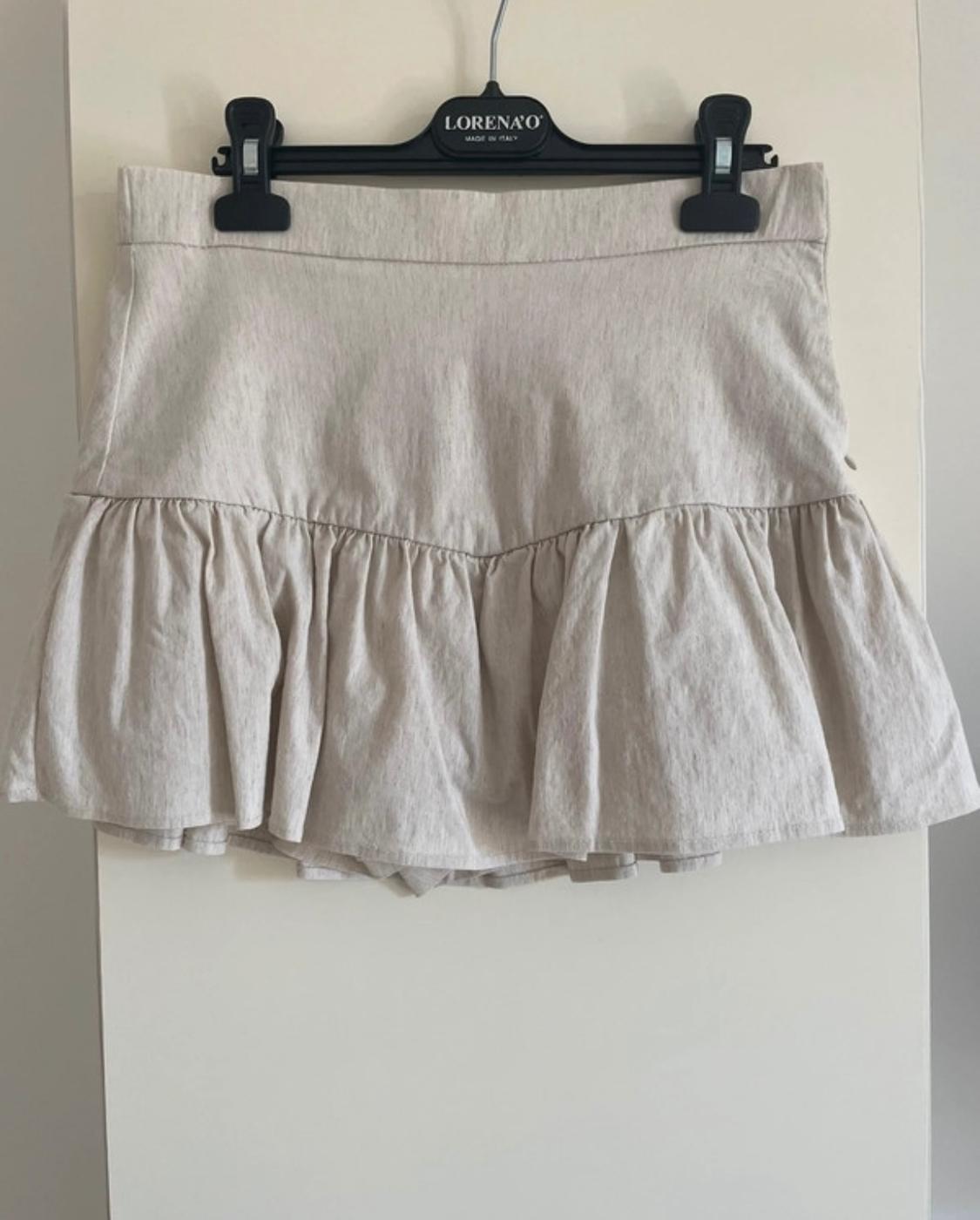 Beige ruffled skirt hanging on a black hanger with the "LORENA'O" brand visible. Plain white background.