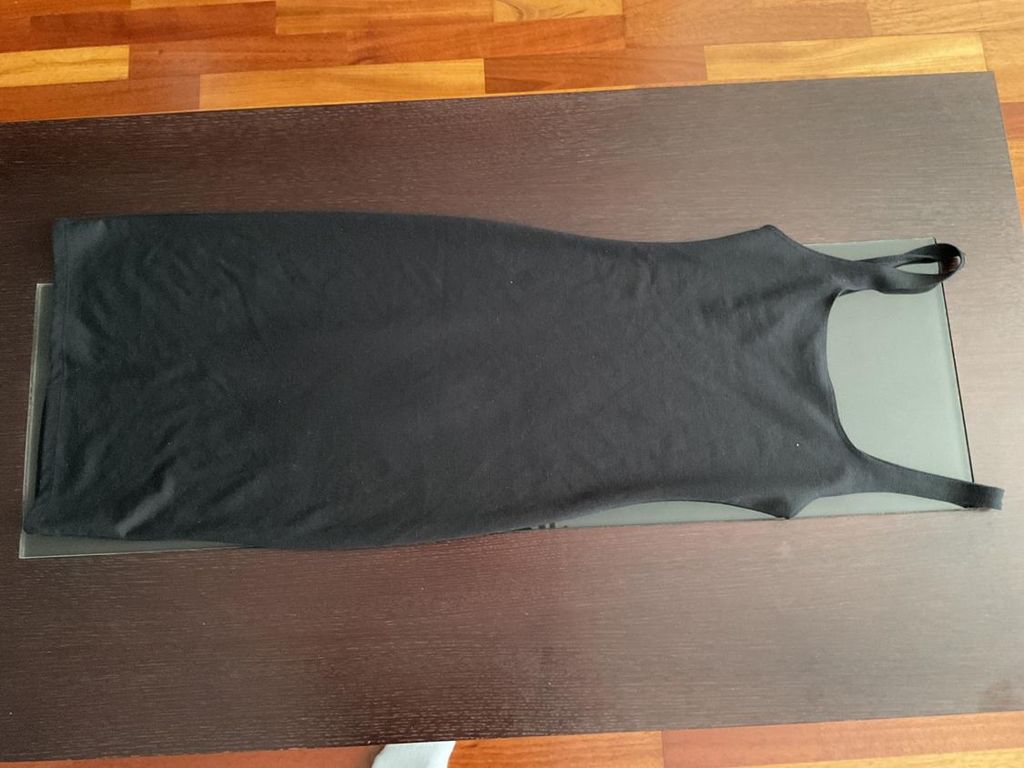 Sleeveless black dress on a dark wooden table, viewed from above. Light wooden floor background.