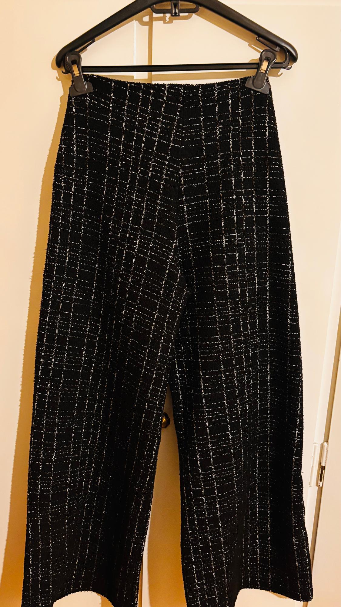 Black trousers with a white linear pattern hanging on a black hanger against a light background.