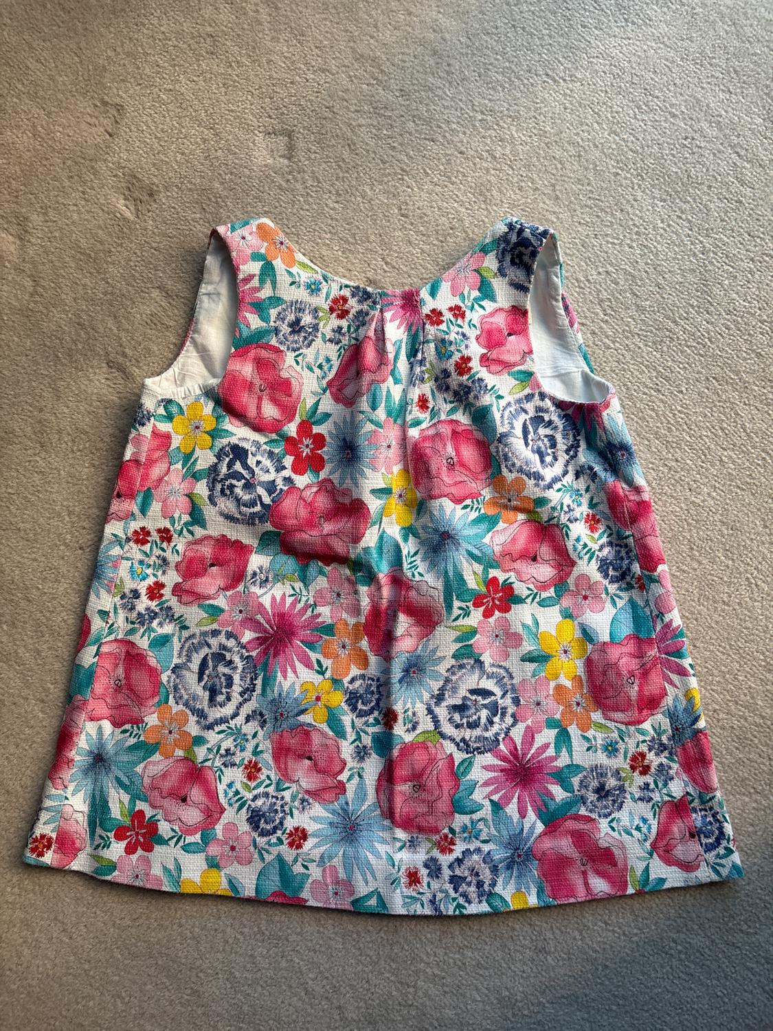 Sleeveless dress with colourful floral print on a light background, placed on a beige surface.