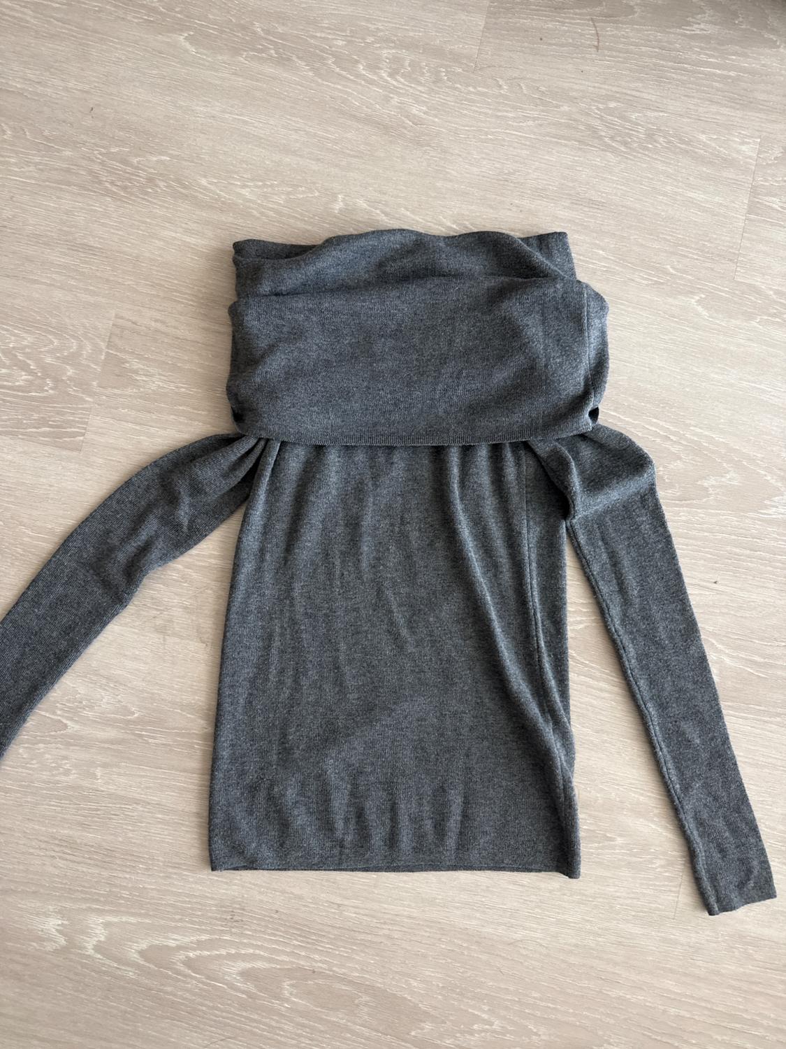 Dark gray knit sweater, long sleeves and a wide folded collar, presented on a light wood floor. Casual style.
