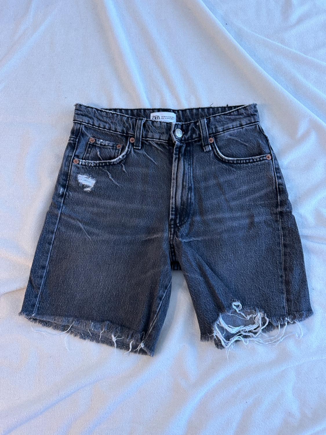 Distressed denim shorts with frayed hem on white fabric. Visible label on the waistband.