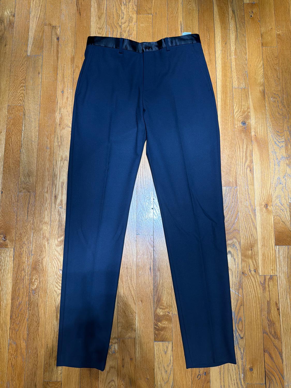 Dark blue trousers with a satin waistband, placed on a light wooden floor.