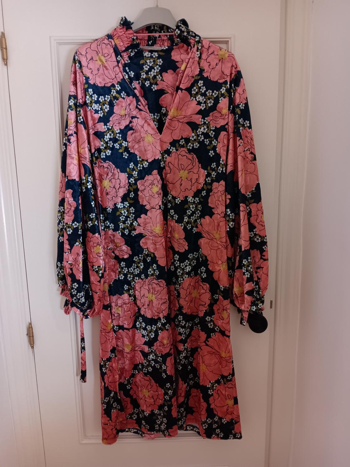 Long-sleeved maxi dress with a floral print in pink tones and a dark blue background, hanging on a white door.