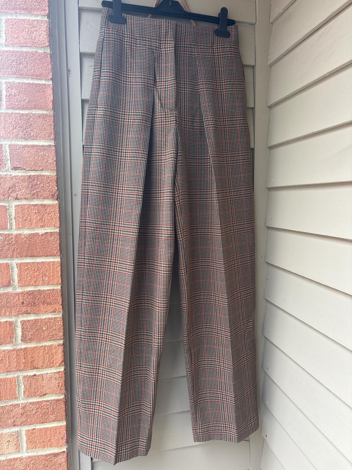 Checked trousers hanging on a black hanger, with a red brick background and white cladding.