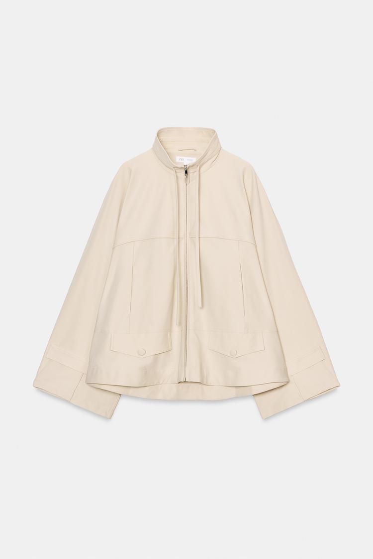 P�edn� pohled na tmav� b�ovou bundu s nastaviteln�m vysok�m l�mcem, kovov�m zipem, dlouh�mi ruk�vy a kapsami s klopou a knofl�kem.