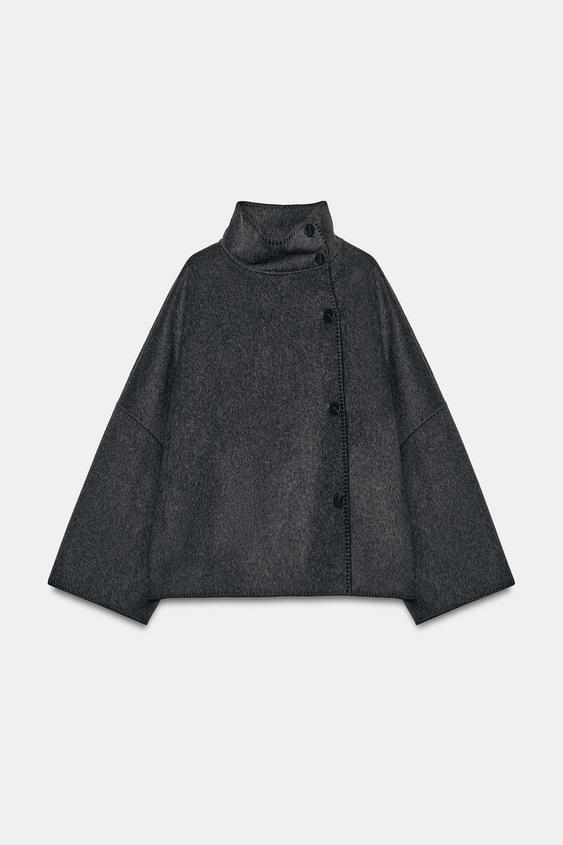Přední pohled na tmavě šedou bundu s vysokým límcem, širokými dlouhými rukávy a zapínáním na knoflíky vpředu. Skryté boční kapsy.
