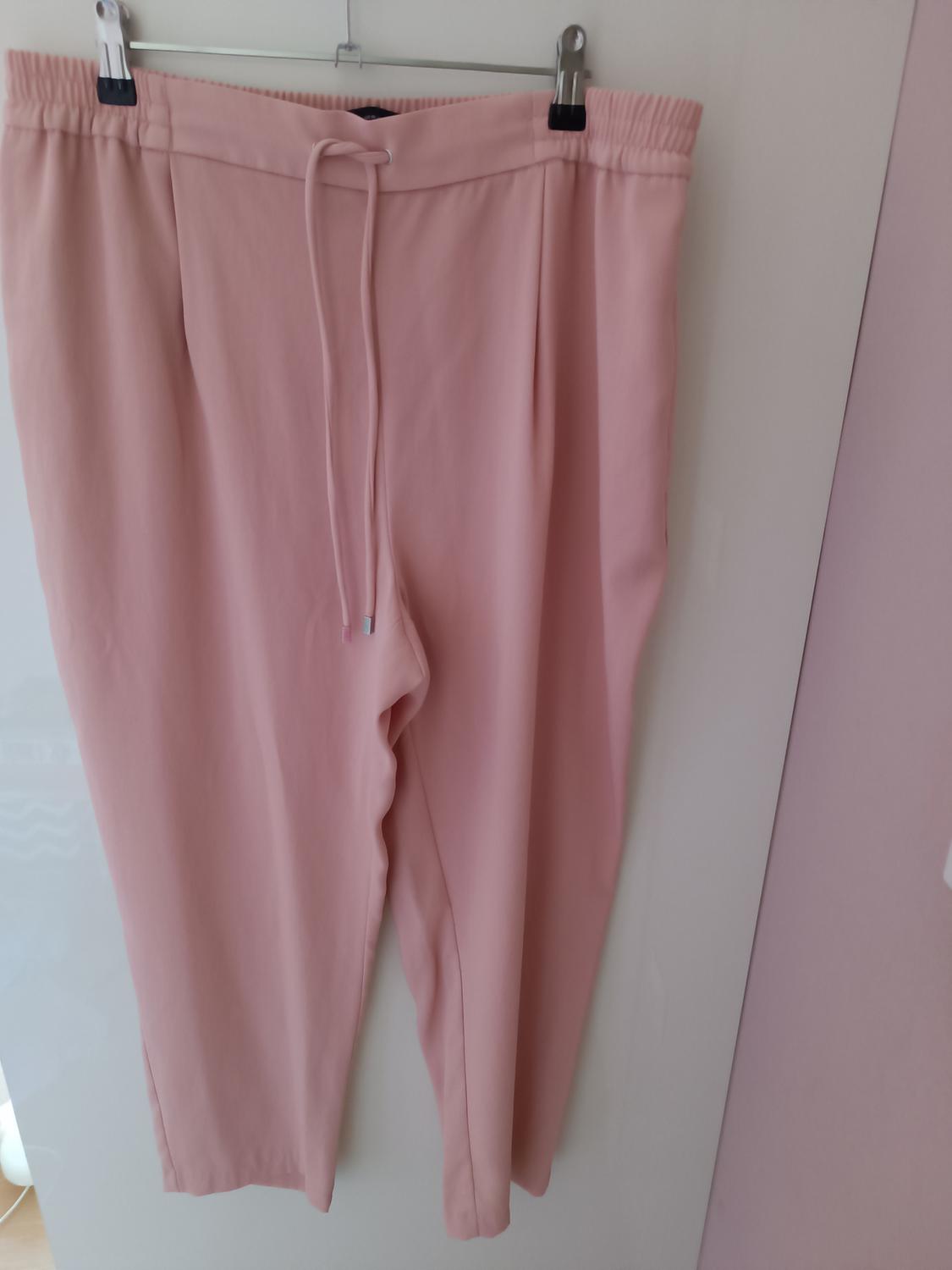 Pink trousers hanging on a hanger with adjustable drawstring at the waist, against a white and light pink background.