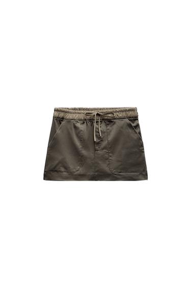 Front view of a brown mini skirt with an elasticated waistband and front pockets.